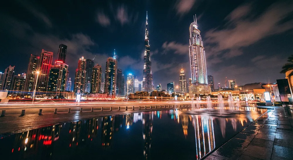 Burj Khalifa and Downtown Dubai skyline at night reflected in the Dubai Fountain pool