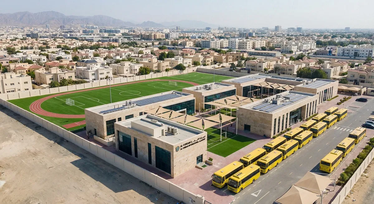 Aerial view of a private school campus in a Middle Eastern city with sports fields and school buses