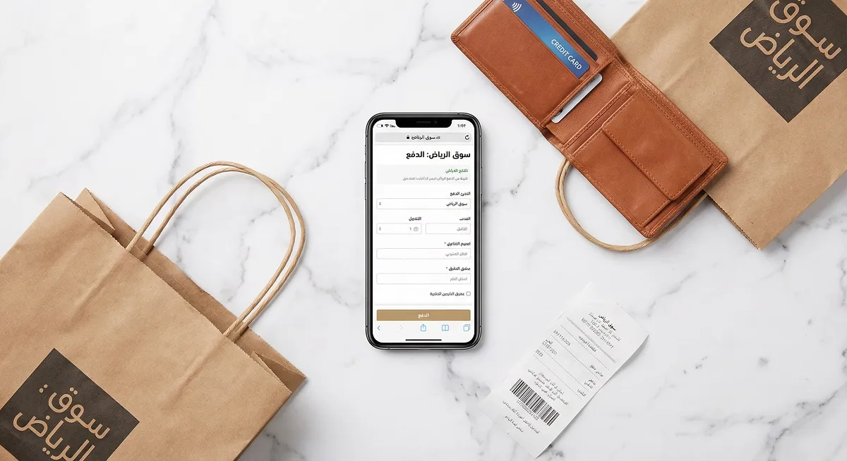 Arabic e-commerce checkout page on smartphone with Saudi shopping bags on marble surface