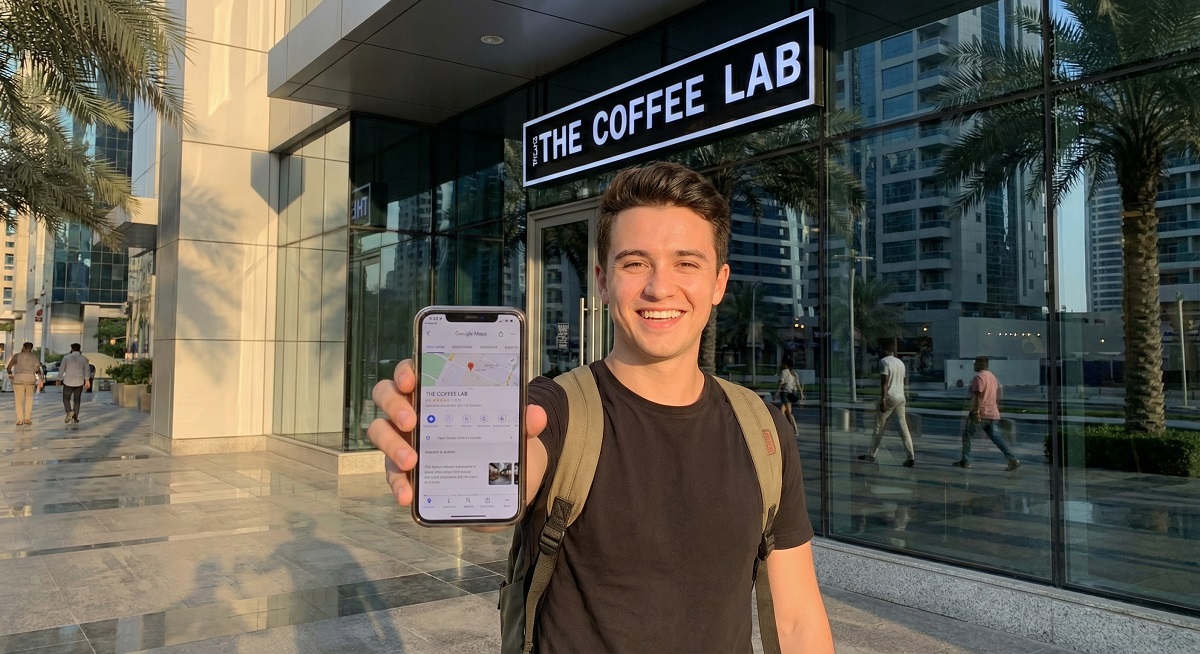 Business owner in JLT Dubai viewing their Google Maps listing on smartphone outside their storefront