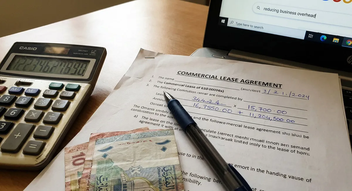 Commercial lease agreement with calculator and Omani rial banknotes beside laptop showing Google search page
